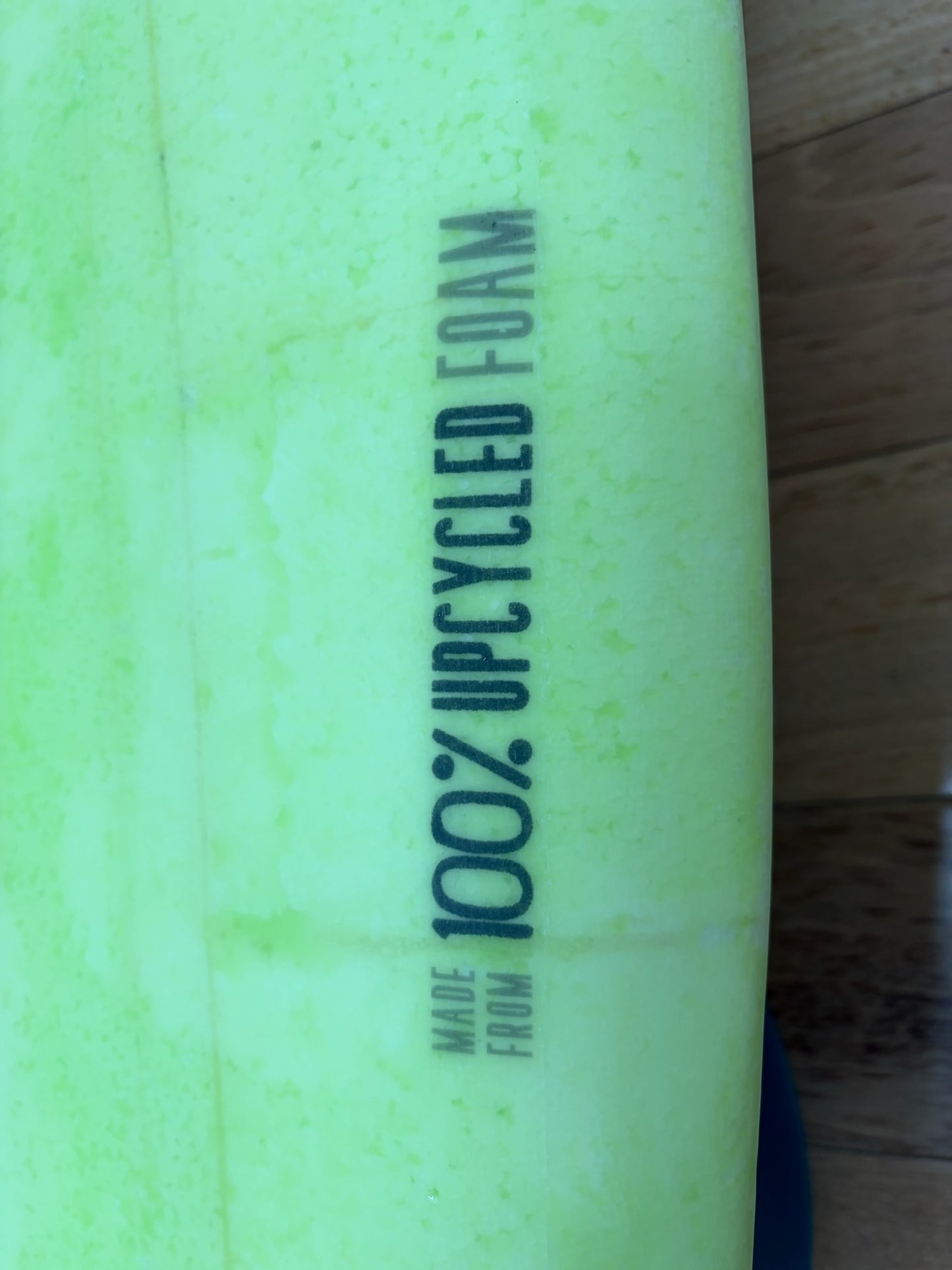 Close-up of a bright lime green surfboard with vertical printed text reading 'Made from 100% UPCYCLED FOAM'