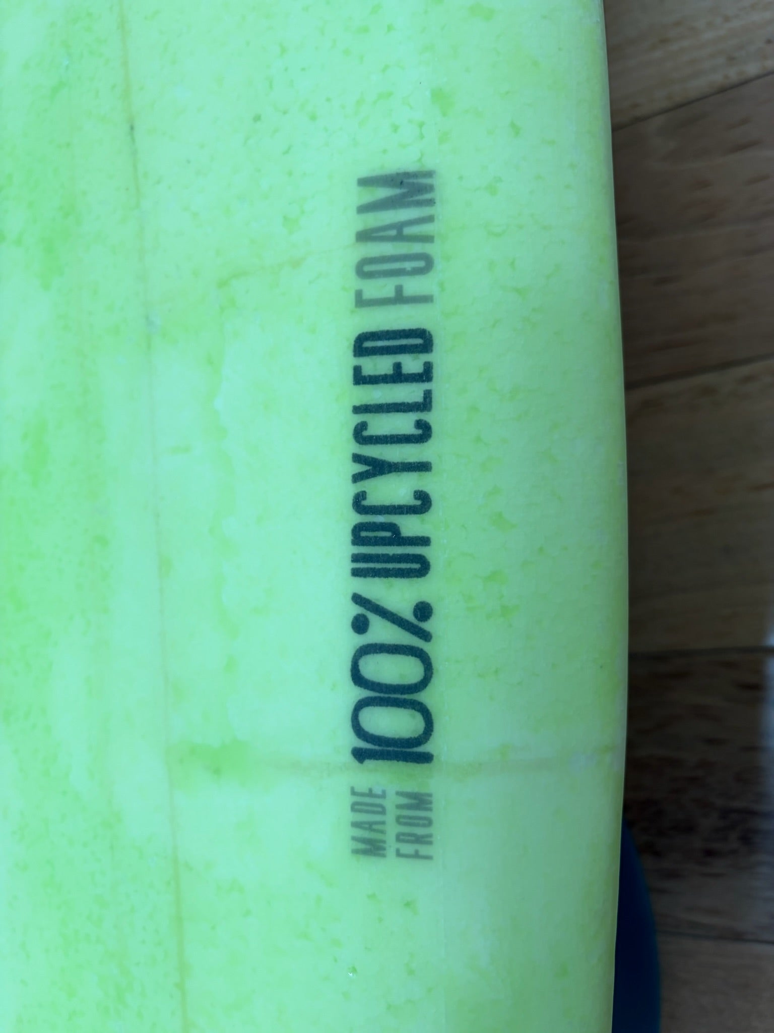 Close-up of a bright lime green surfboard with vertical printed text reading 'Made from 100% UPCYCLED FOAM' 