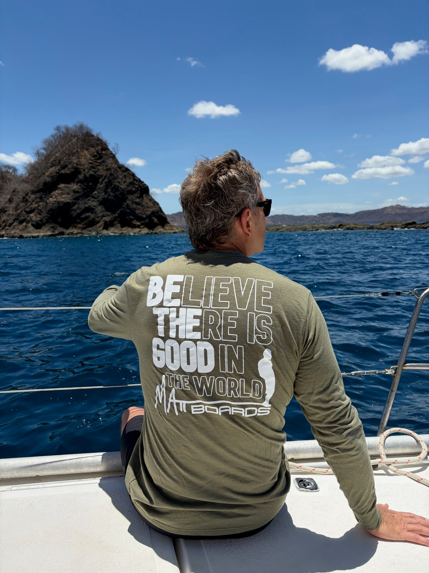 Person on a boat wearing a shirt with a motivational quote, looking out at the ocean.