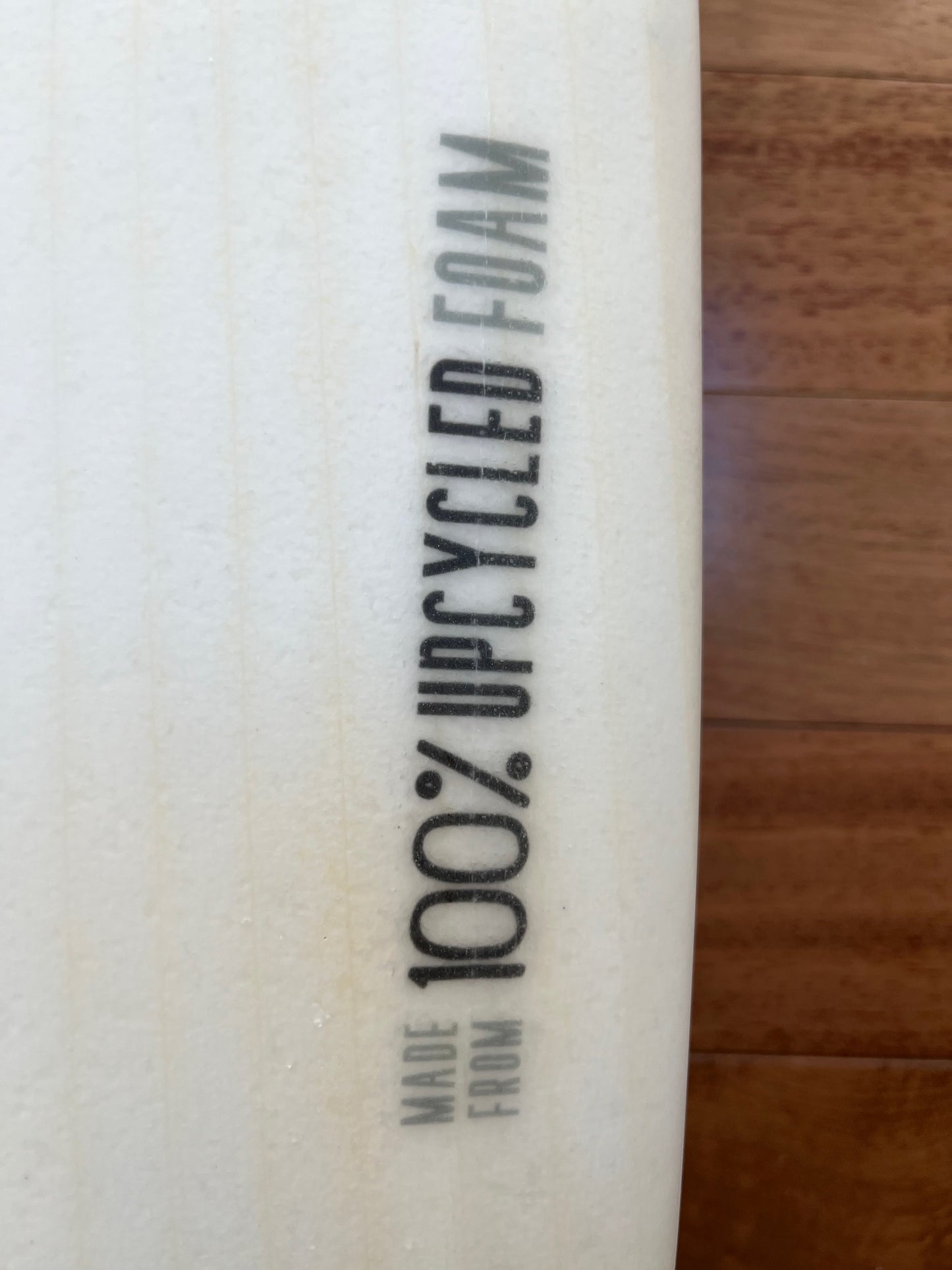 Close up of white surfboard showing detail of graphic that says "Made from 100% upcycled foam"