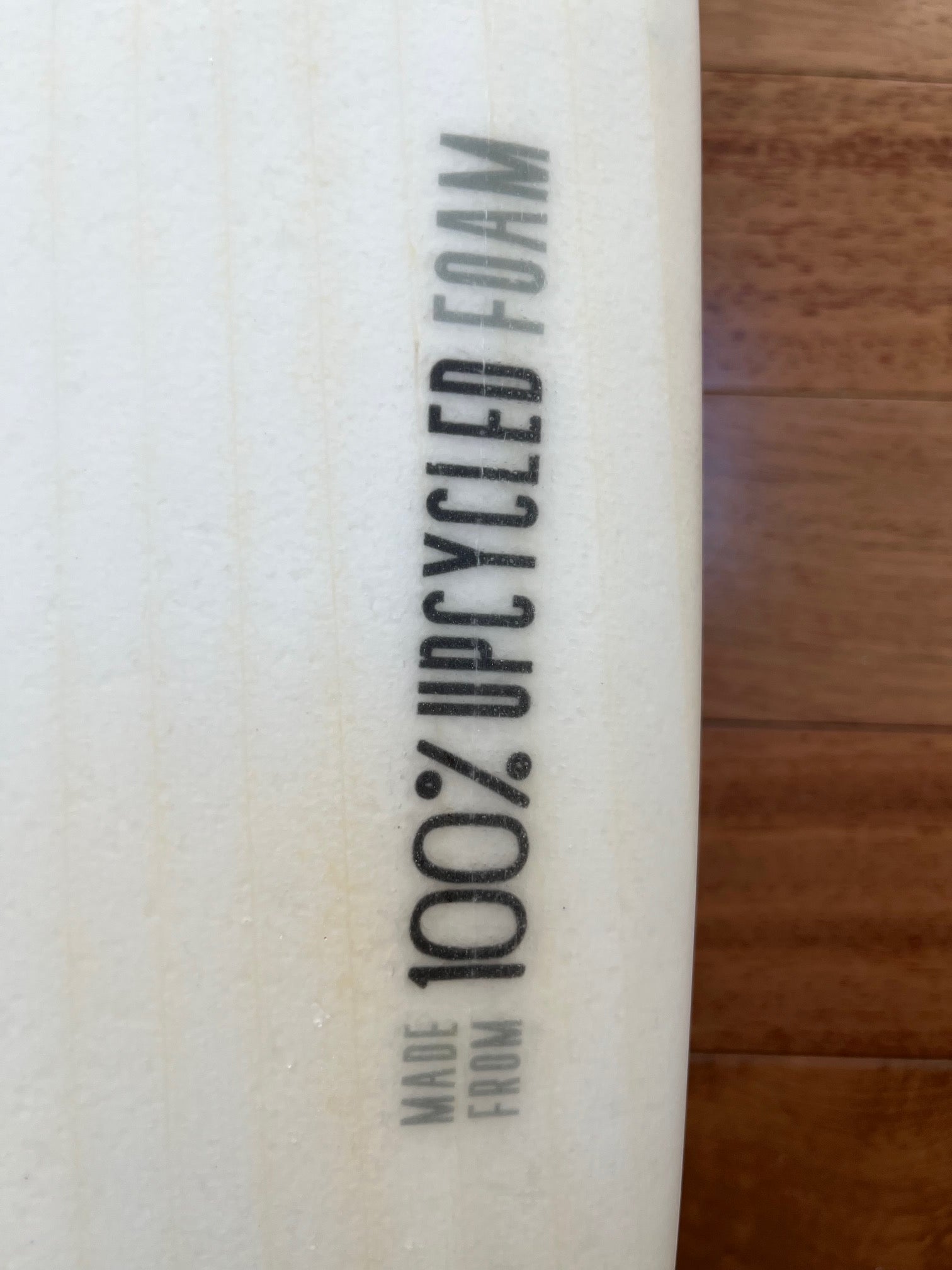 Close up of white surfboard showing detail of graphic that says "Made from 100% upcycled foam"