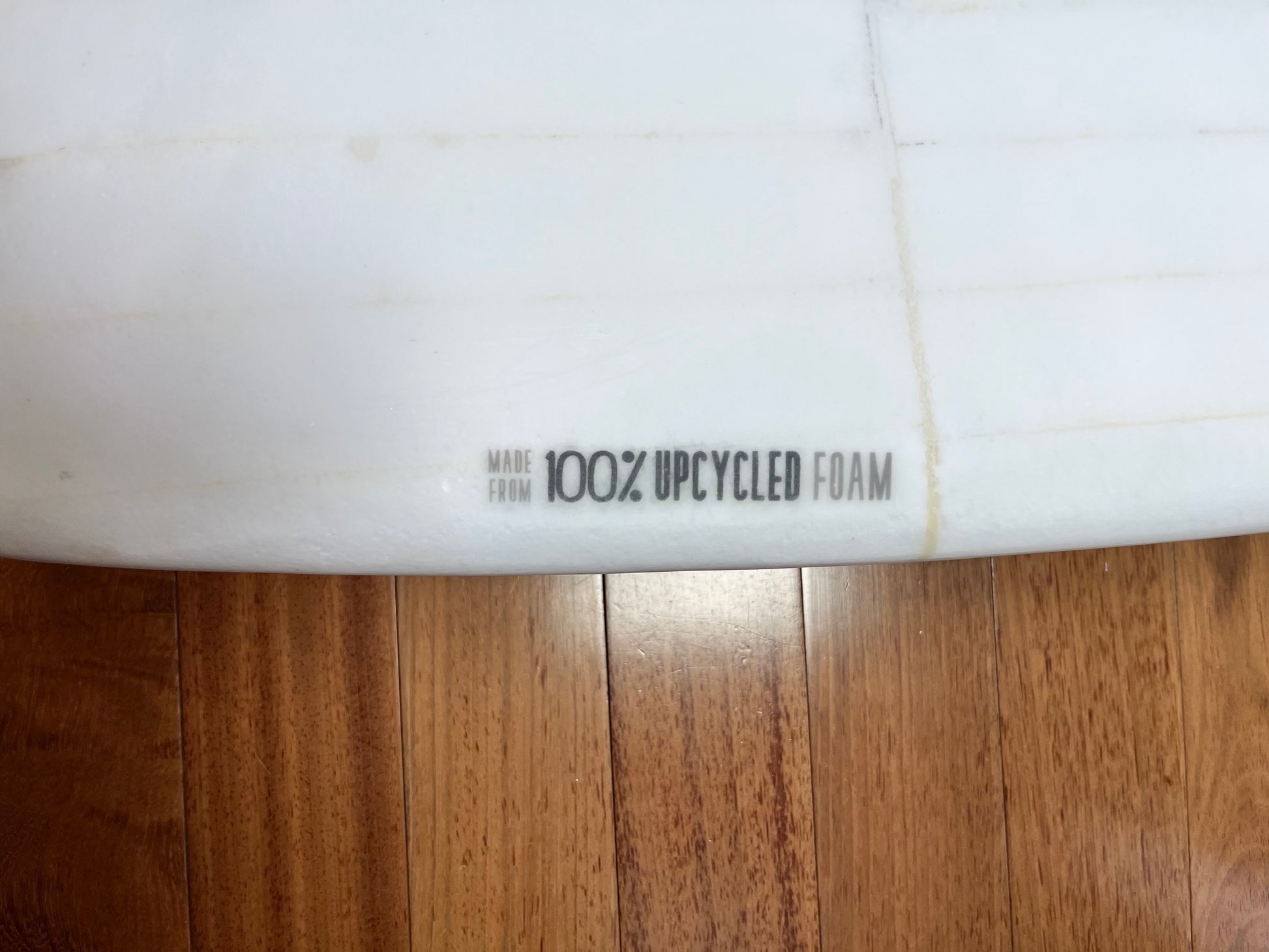 Close-up of a surfboard with 'Made from 100% Upcycled Foam' text on a wooden background