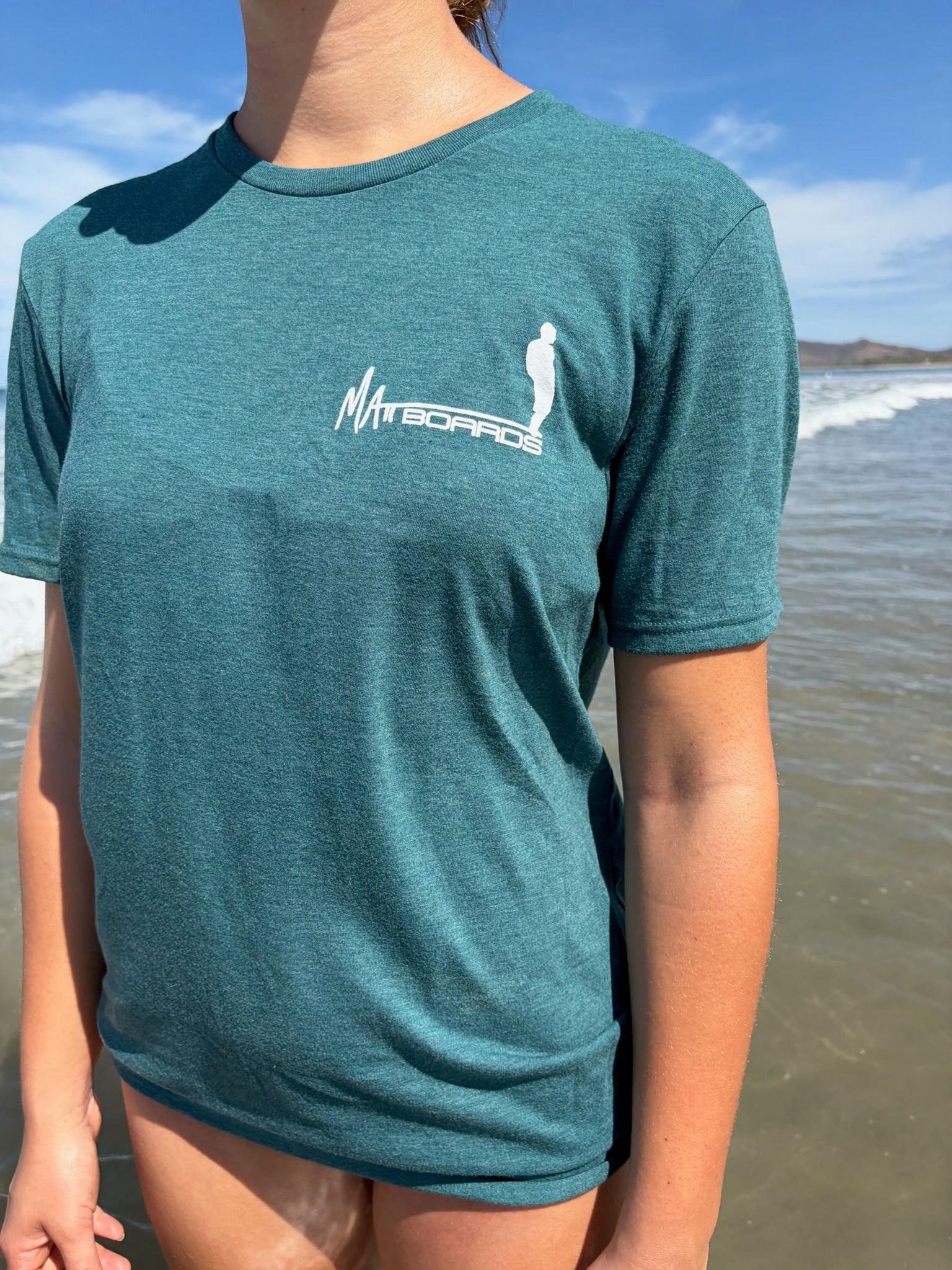 Person wearing a teal t-shirt with a logo on a beach
