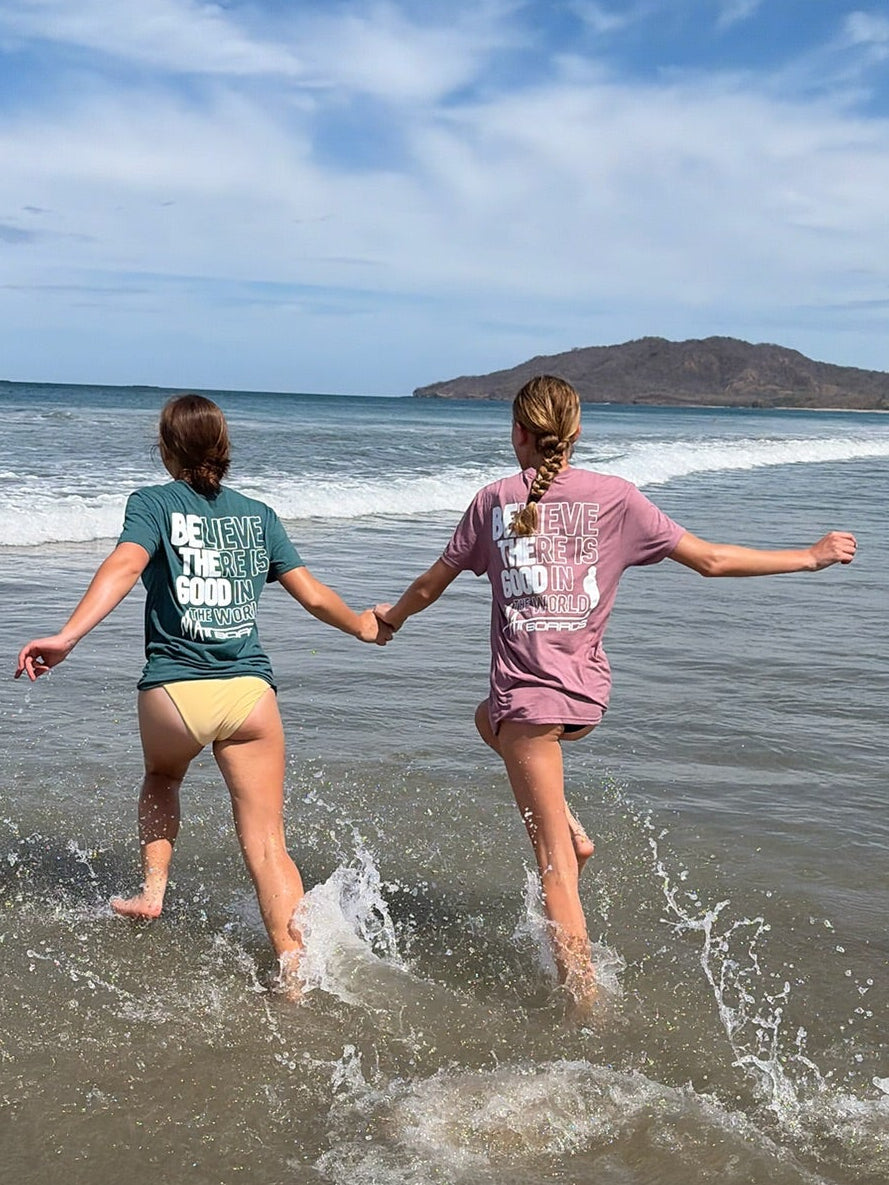 Two people holding hands and walking into the ocean with a clear sky and distant island.