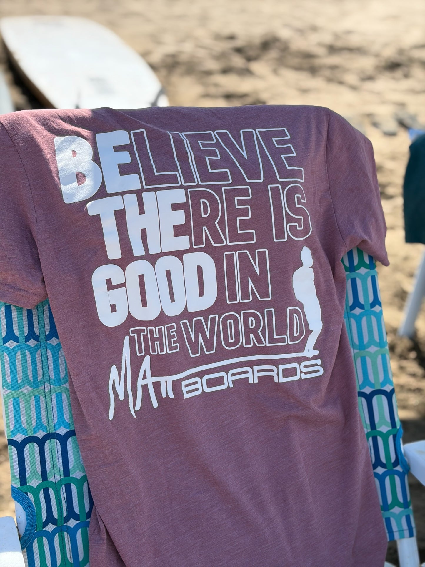 Rose colored t-shirt with motivational quote and brand logo on a beach chair